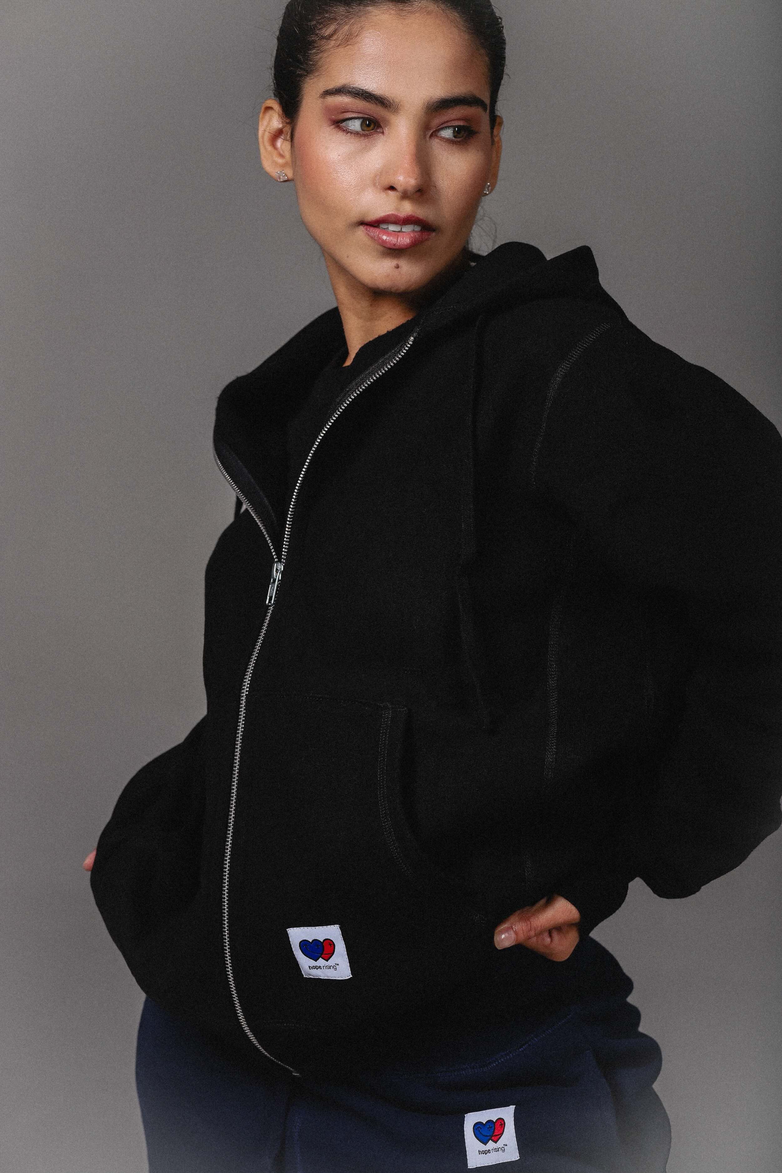 Person wearing a black hoodie with visible brand logos on a gray background
