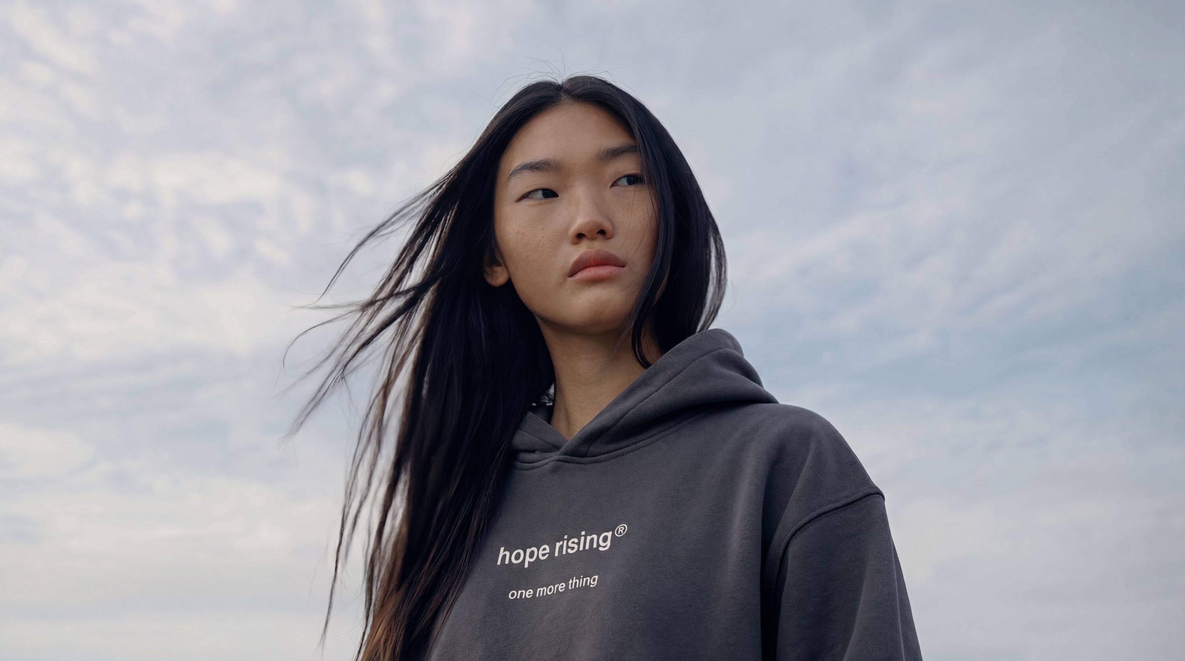 Person wearing a hoodie with 'hope rising' text against a cloudy sky